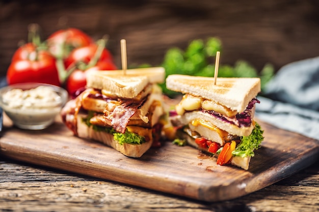 Sandwich di pollo e formaggio con cavolo rosso, peperoni e insalata in ambiente rustico in legno.