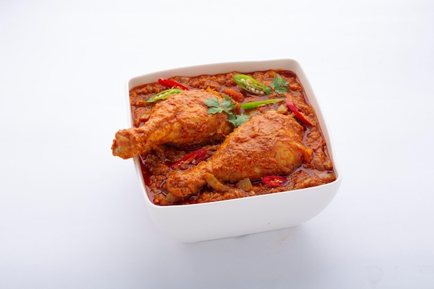 Chicken curry or masala , spicy reddish chicken leg piece dish garnished with coriander leaf and  fresh green chilli which is arranged in a white ceramic bowl with white background,isolated.