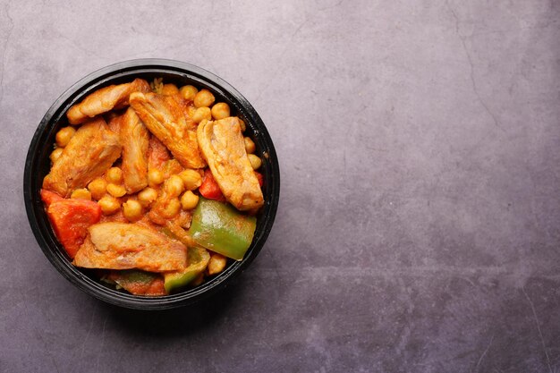 Chicken curry mixed with vegetables in a bowl on black