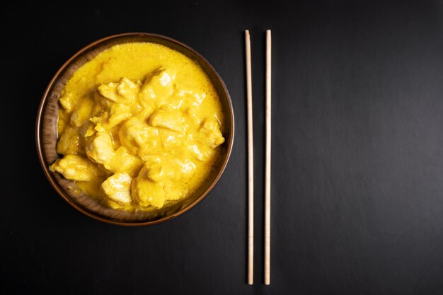 Chicken in curry sauce with chopsticks on a black background Top view