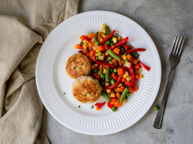 Cotolette di pollo con verdure miste al vapore, polpette di pollo sul piatto bianco.