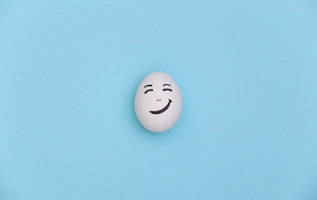 Chicken egg with hand drawn happy face on a blue background.