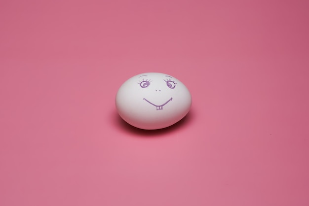 Chicken egg with painted face smiling emoticon on a pink background. Easter. High quality photo