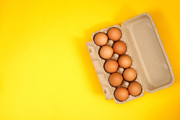 Chicken eggs in a cardboard box ready to cook on a yellow background