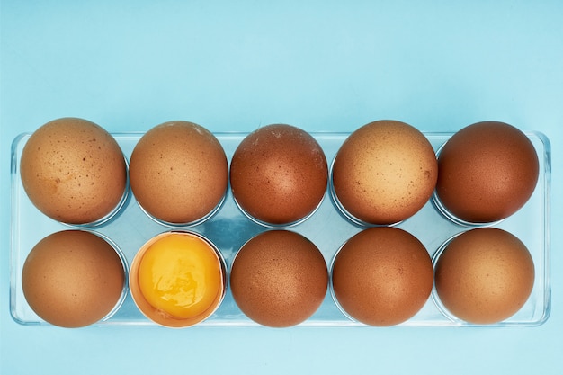Chicken eggs in an egg holder. full tray of eggs. half an egg,\
egg yolk, shell.