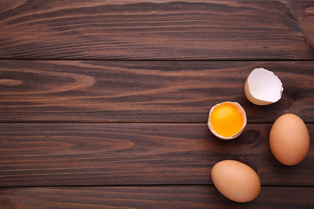 Chicken eggs and half with yolk on a brown background.