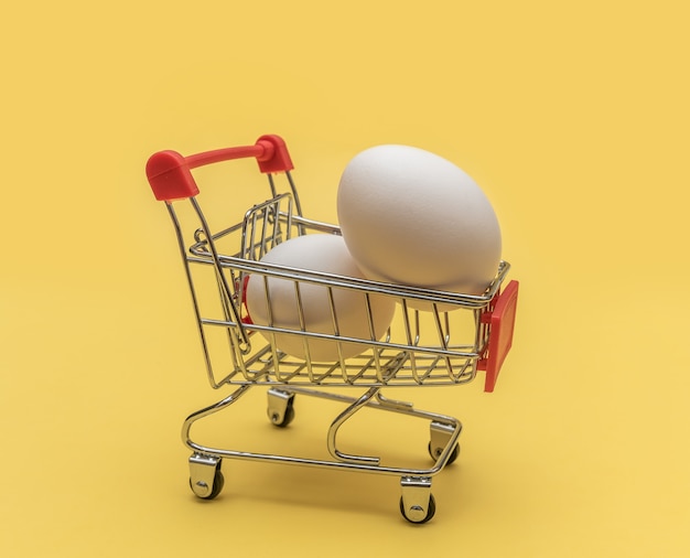 Chicken eggs in a mini grocery cart on a yellow wall. Close-up.