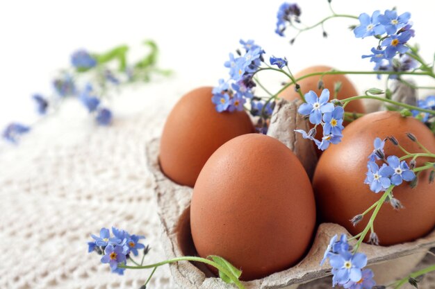 Chicken eggs in a package on a white napkin with forgetmenots white background closeup