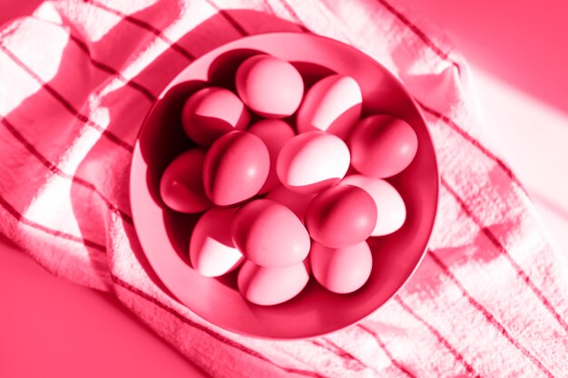 Chicken eggs pink color in a purple plate on a checked kitchen towel on a magenta table concept farm products and natural nutrition toned in viva magenta trend color of the year 2023