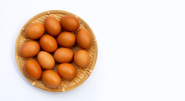 Chicken eggs in round bamboo basket on white.