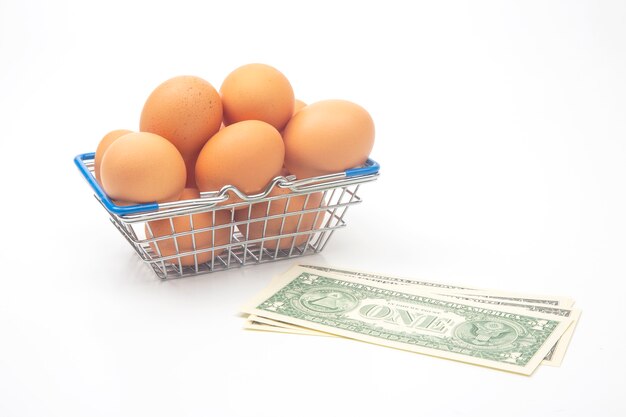 Chicken eggs in a supermarket grocery basket and dollars on a white background. sale and business of food products