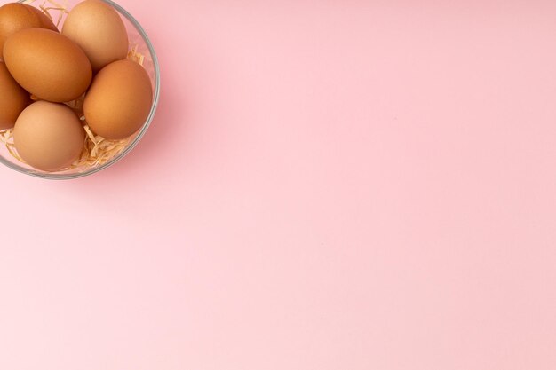 Chicken eggs in a transparent plate on a pink background