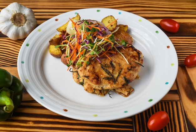 Chicken fillet served with potatoes vegetables and sauce on white plate close up side view