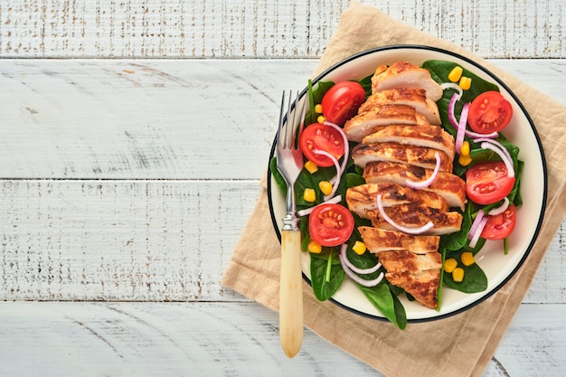 Filetto di pollo con insalata di spinaci, pomodorini, fiordaliso e cipolla. cibo salutare. dieta cheto, concetto di pranzo dietetico. vista dall'alto su sfondo bianco.