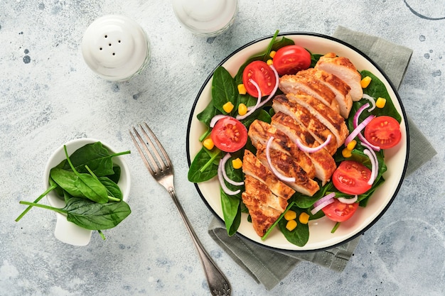 Filetto di pollo con insalata di spinaci, pomodorini, fiordaliso e cipolla. cibo salutare. dieta cheto, concetto di pranzo dietetico. vista dall'alto su superficie bianca.