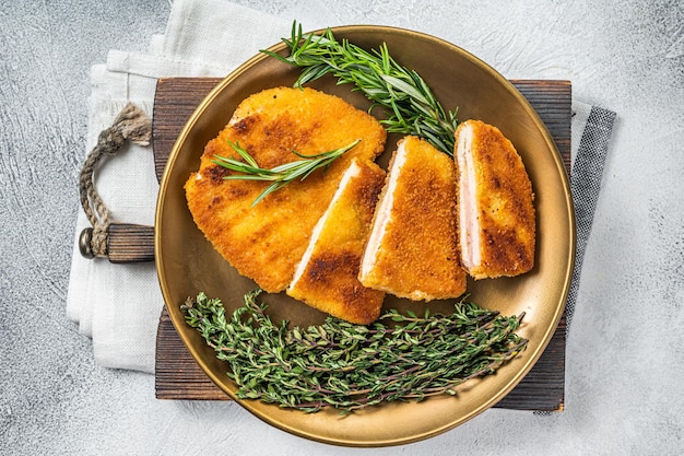 Chicken fried Cordon bleu cutlet with ham and cheese on a plate with herbs White background Top view