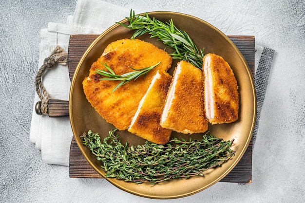 Куриная жареная котлета Cordon bleu с ветчиной и сыром на тарелке с зеленью Белый фон Вид сверху