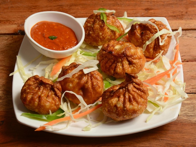 Chicken fried momo with sauce served over a rustic wooden background selective focus