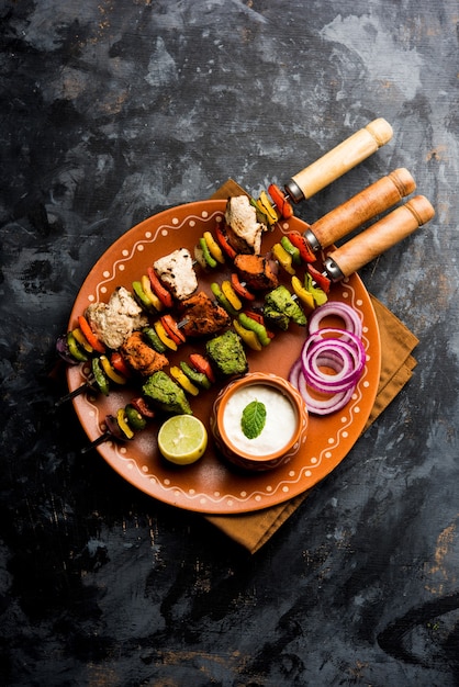 Chicken Hariyali kakab or Malai malai kebab in tricolour served with skewers and yogurt dip in a plate