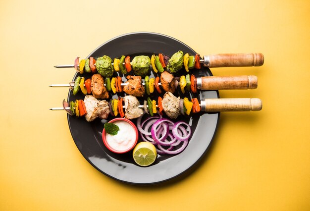 Chicken Hariyali kakab or Malai malai kebab in tricolour served with skewers and yogurt dip in a plate