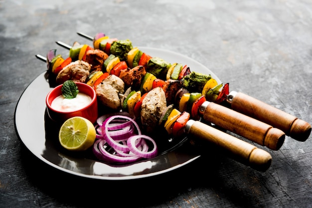 Chicken Hariyali kakab or Malai malai kebab in tricolour served with skewers and yogurt dip in a plate