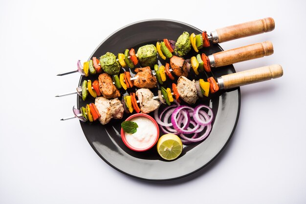 Chicken Hariyali kakab or Malai malai kebab in tricolour served with skewers and yogurt dip in a plate