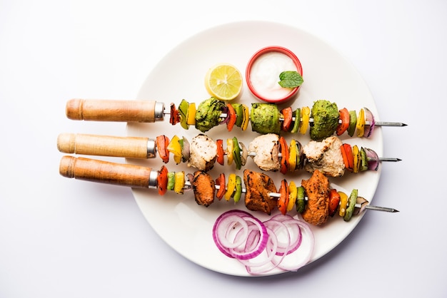 Chicken Hariyali kakab or Malai malai kebab in tricolour served with skewers and yogurt dip in a plate