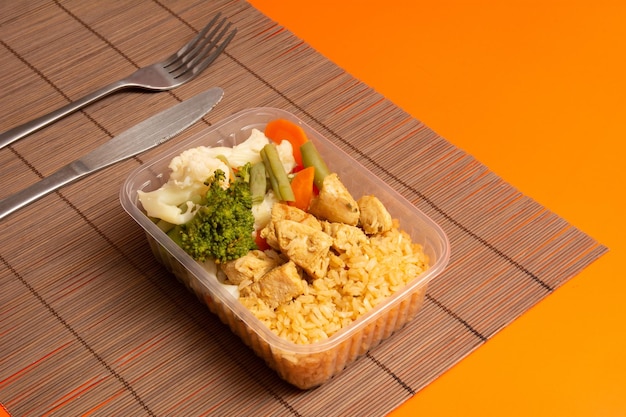 Photo chicken healthy packed lunch box in aerial view clean orange and wood place mat background