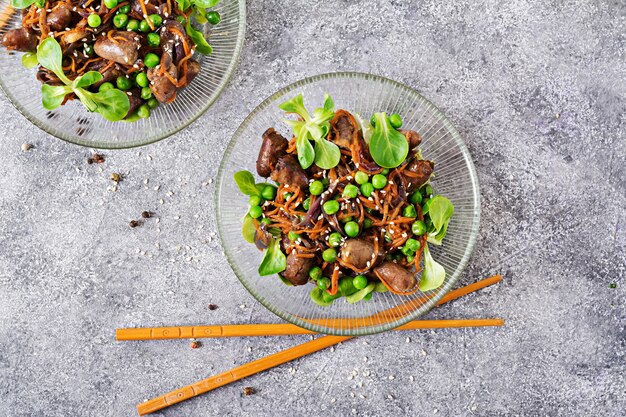 Chicken hearts with carrots, onions and green peas in Asian style. Top view