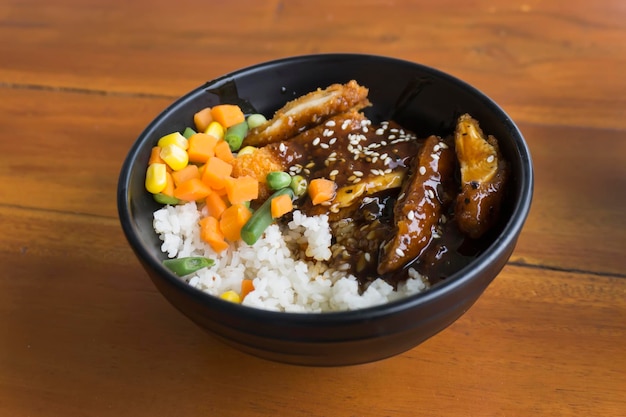 Chicken katsu rice bowl with vegetables and corn on wooden background