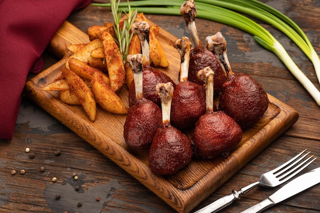 튀긴 감자와 함께 향신료로 구운 닭 다리, 나무 판자 위에 있는 꼭대기. 말린 후추 열매. 나무 배경입니다. 파.