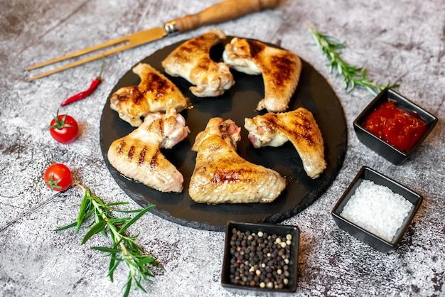 Chicken legs on a black plate with spices and herbs.