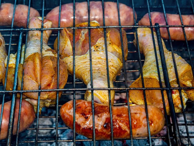 Chicken legs and meat sausages on an iron grill mesh