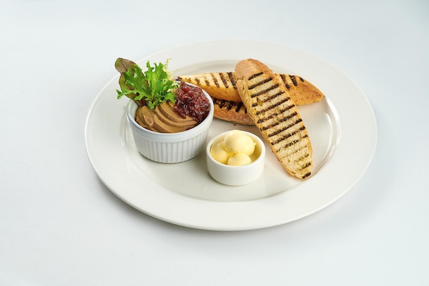 Chicken liver pate with toast and onion confit in a white plate on a white tablecloth