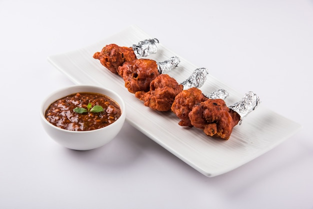 Photo chicken lollipop is indian chinese appetizer  which is a frenched chicken winglet. wrapped with silver foil at one end & surved with chutney. over colourful or wooden background. selective focus.