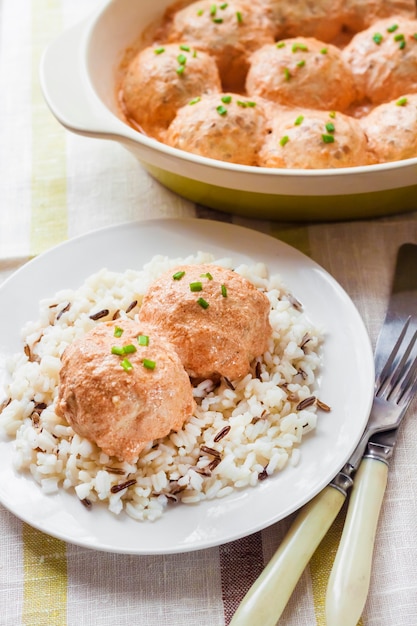 Chicken meatballs in creamy tomato sauce with rice on a white plate