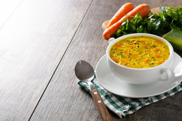 Chicken noodle soup in white bowl on wooden table