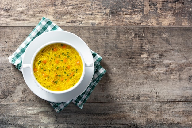 Chicken noodle soup in white bowl on wooden table