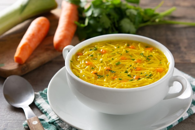 Chicken noodle soup in white bowl on wooden table