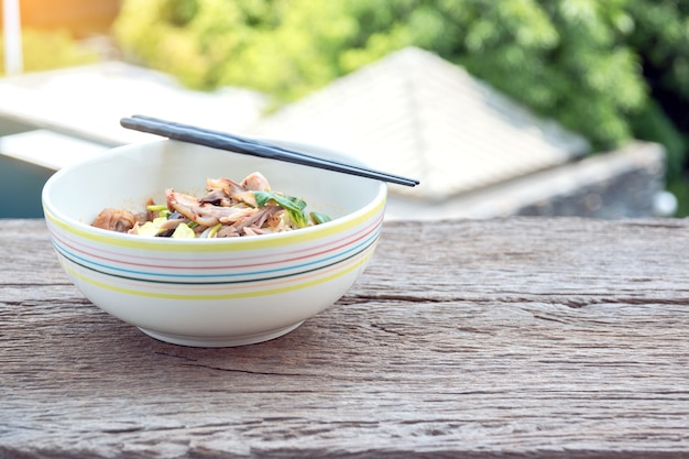 Chicken noodles in a ceramic cup on a wooden table.