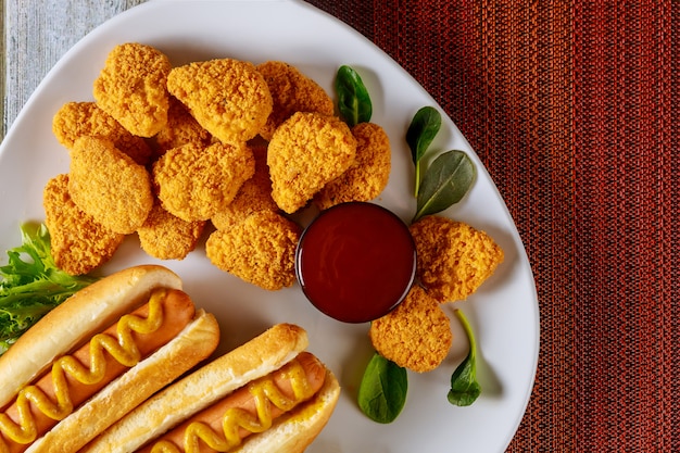 Chicken nuggets and hot dog with mustard on white plate.