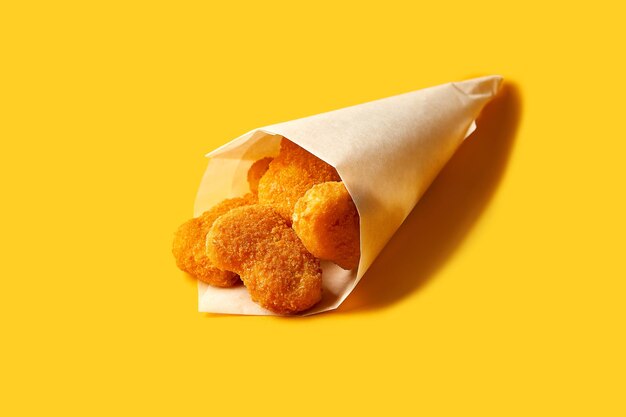 Chicken nuggets in paper on a yellow background. Fast food and finger food for a pub