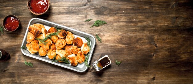 Chicken nuggets on a steel tray with sauce. On a wooden table.