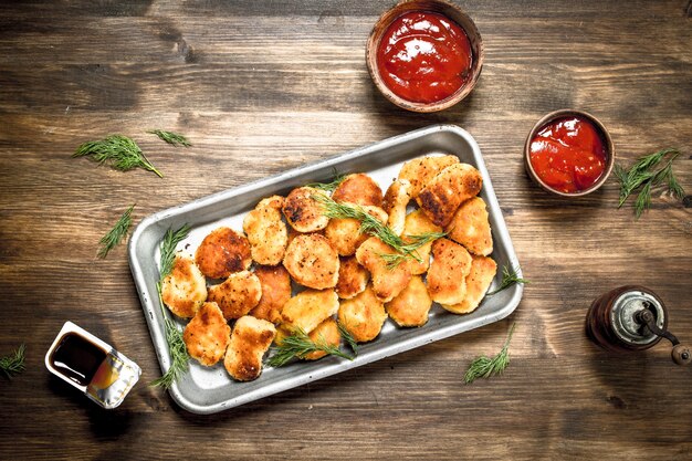 Chicken nuggets on a steel tray with sauce. On a wooden table.