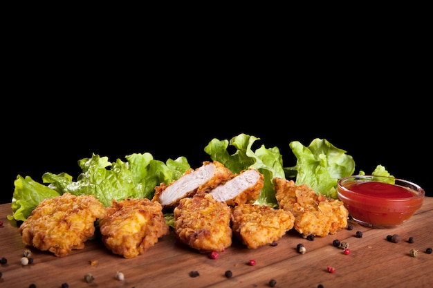 Chicken nuggets, on a wooden table with sauce and lettuce on black background.