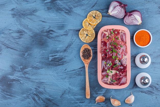 Chicken offal in a wooden plate , spice, salt, spice with spoon garlic and dried lemon, on the blue background. 