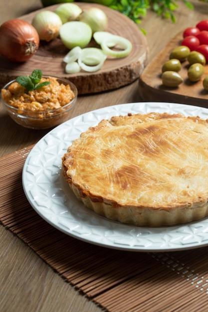 Chicken pie with cottage cheese tomatoes onion and olives on wooden table and white plate