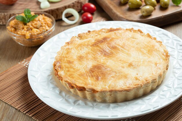 Chicken pie with cottage cheese tomatoes onion and olives on wooden table and white plate