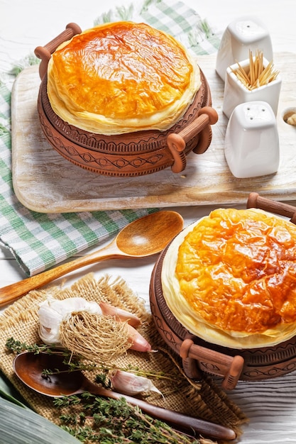 Chicken pot pie in the rustic clay pots on a white wooden table, close-up, vertical view from above, english cuisine