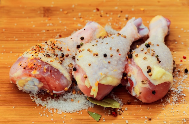 Foto stinco di carne cruda di pollo, bacchette sul tagliere di legno rotondo, spezie per cucinare
